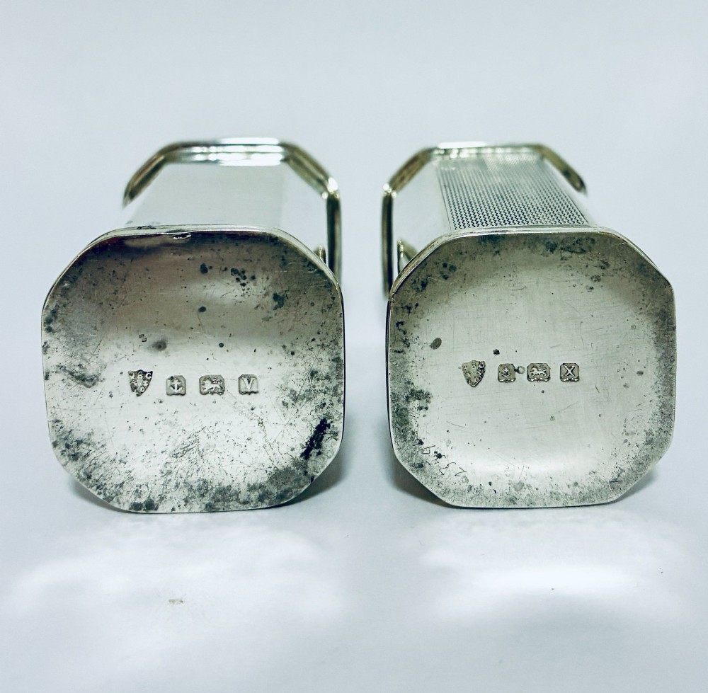 A pair of matching silver pepper pots with canted corners, engine-turned central panels, and perforated tops with decorative finials. View VIII