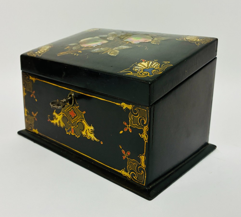 A black lacquered Victorian papier-mache stationery box featuring mother-of-pearl flower inlays on the lid and gilded corner scrollwork around a central brass keyhole. View V