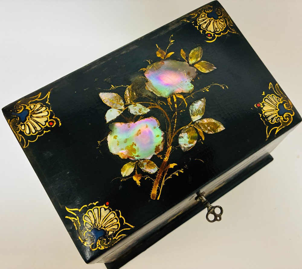 A black lacquered Victorian papier-mache stationery box featuring mother-of-pearl flower inlays on the lid and gilded corner scrollwork around a central brass keyhole. View X