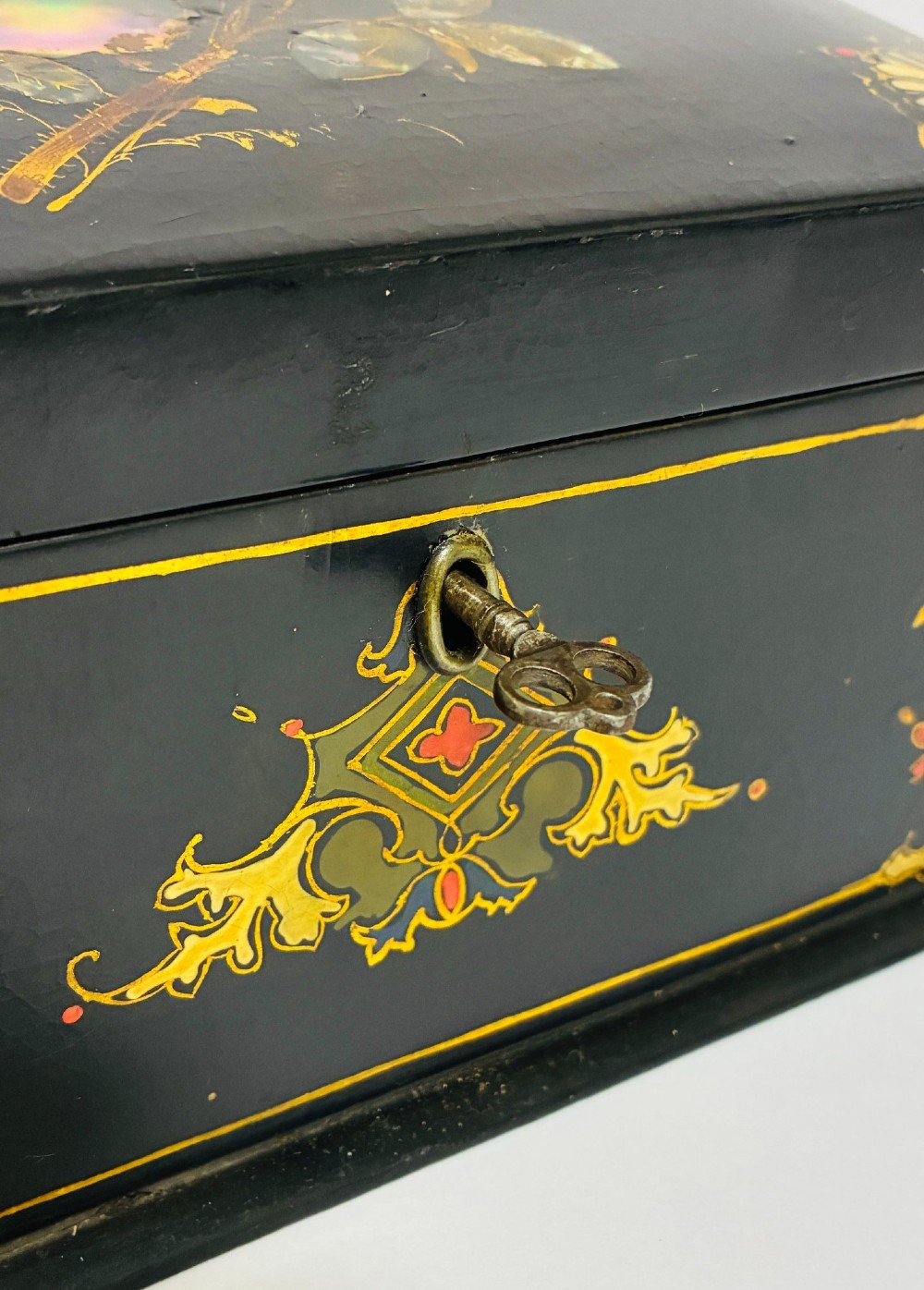A black lacquered Victorian papier-mache stationery box featuring mother-of-pearl flower inlays on the lid and gilded corner scrollwork around a central brass keyhole. View XI