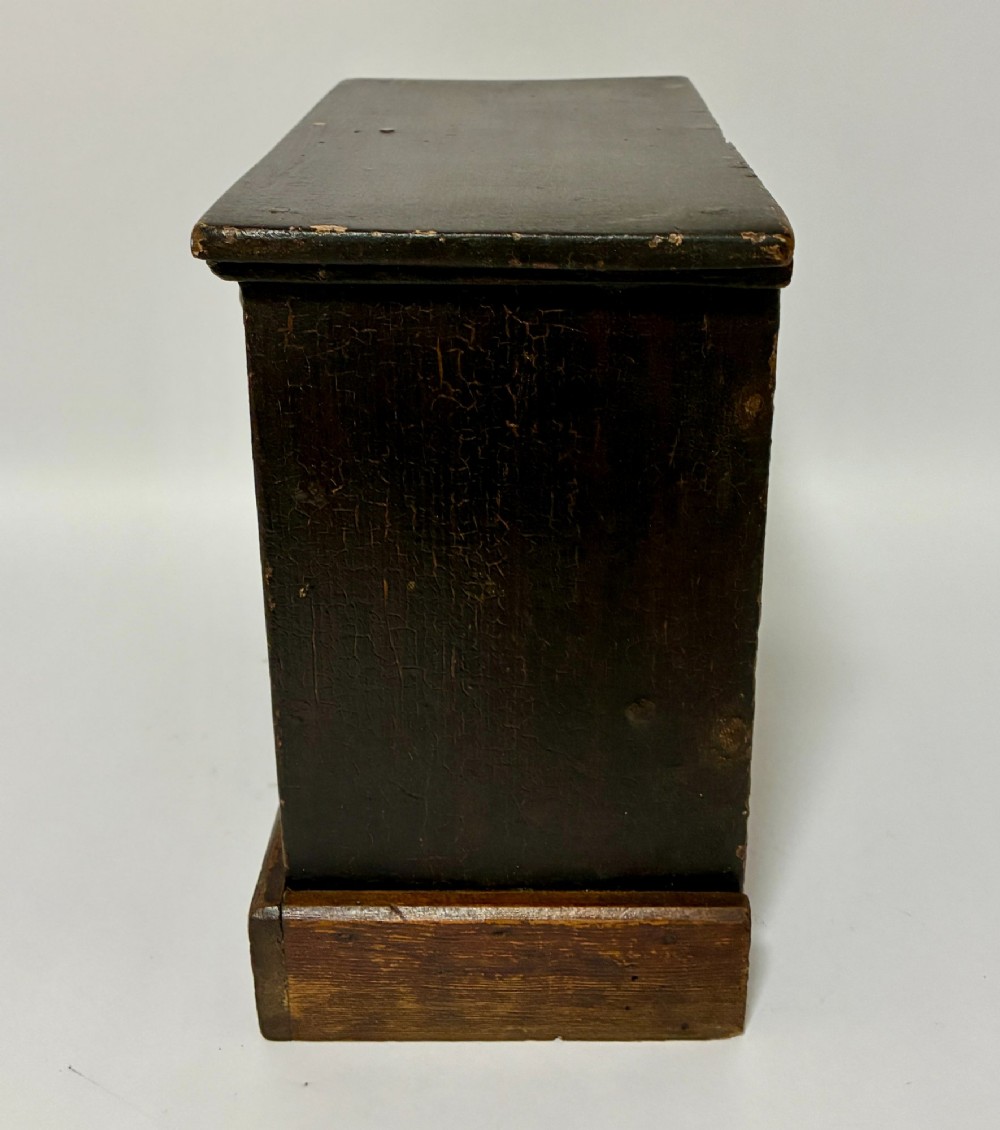 A small wooden miniature chest of drawers featuring two small upper drawers and two full-width lower drawers with turned brass knobs. View IV