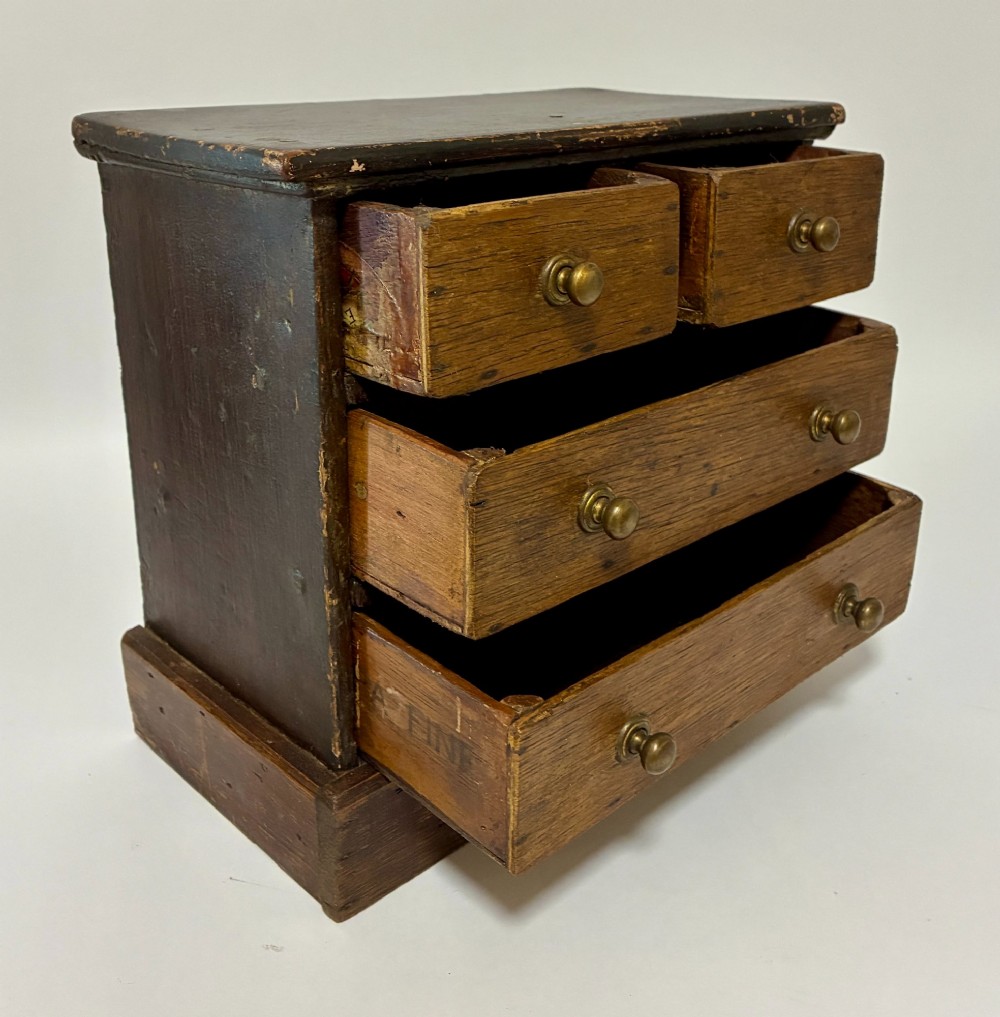 A small wooden miniature chest of drawers featuring two small upper drawers and two full-width lower drawers with turned brass knobs. View VIII