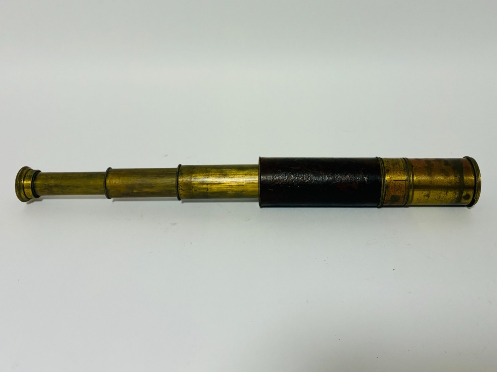 An extended three-draw antique brass pocket telescope featuring a dark brown textured leather barrel wrap.