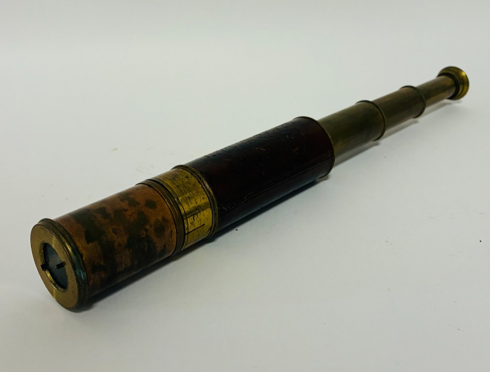 An extended three-draw antique brass pocket telescope featuring a dark brown textured leather barrel wrap. View II