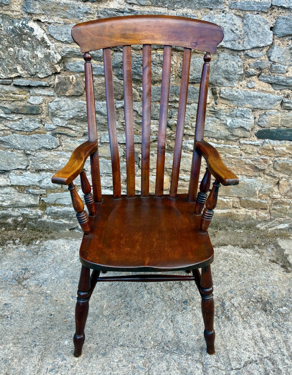 A Victorian country lath back armchair in warm brown wood, featuring vertical back slats, curved armrests, a contoured seat, and turned legs.