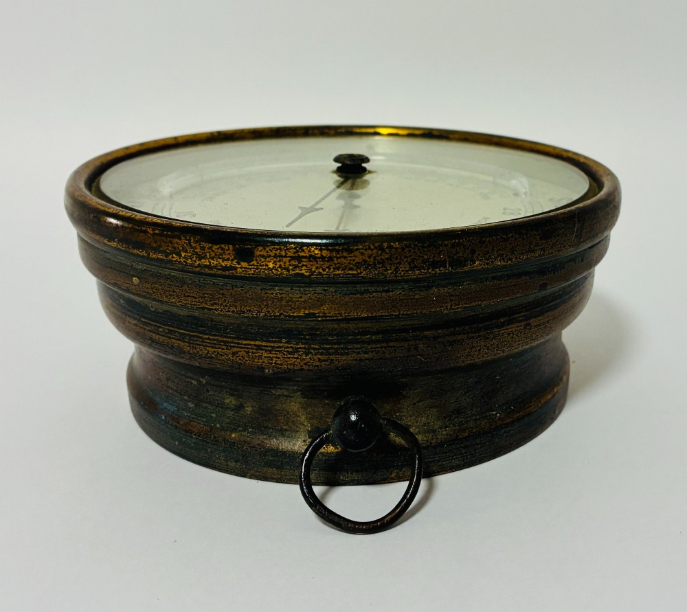 A circular antique brass wall barometer with a cream dial displaying weather conditions and an integrated glass tube thermometer. View IV