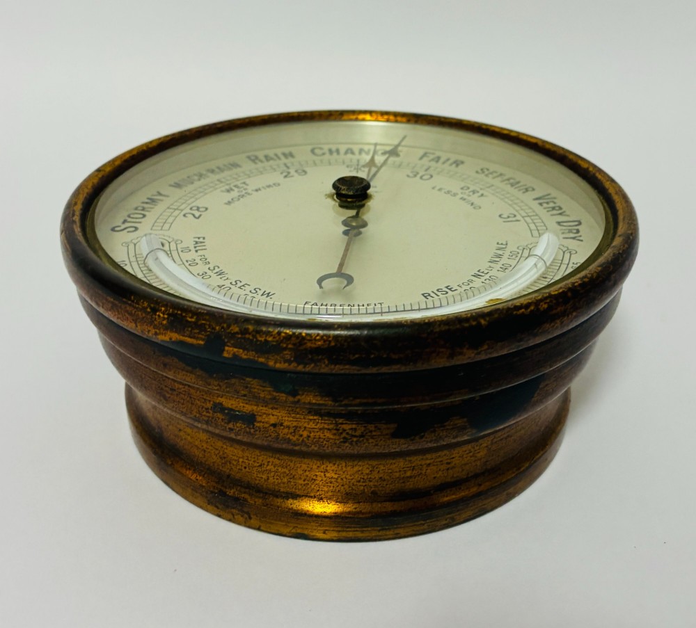 A circular antique brass wall barometer with a cream dial displaying weather conditions and an integrated glass tube thermometer. View VI