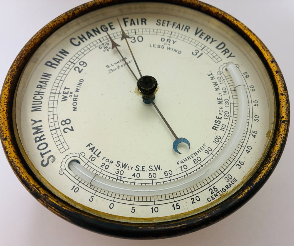A circular antique brass wall barometer with a cream dial displaying weather conditions and an integrated glass tube thermometer. View VIII