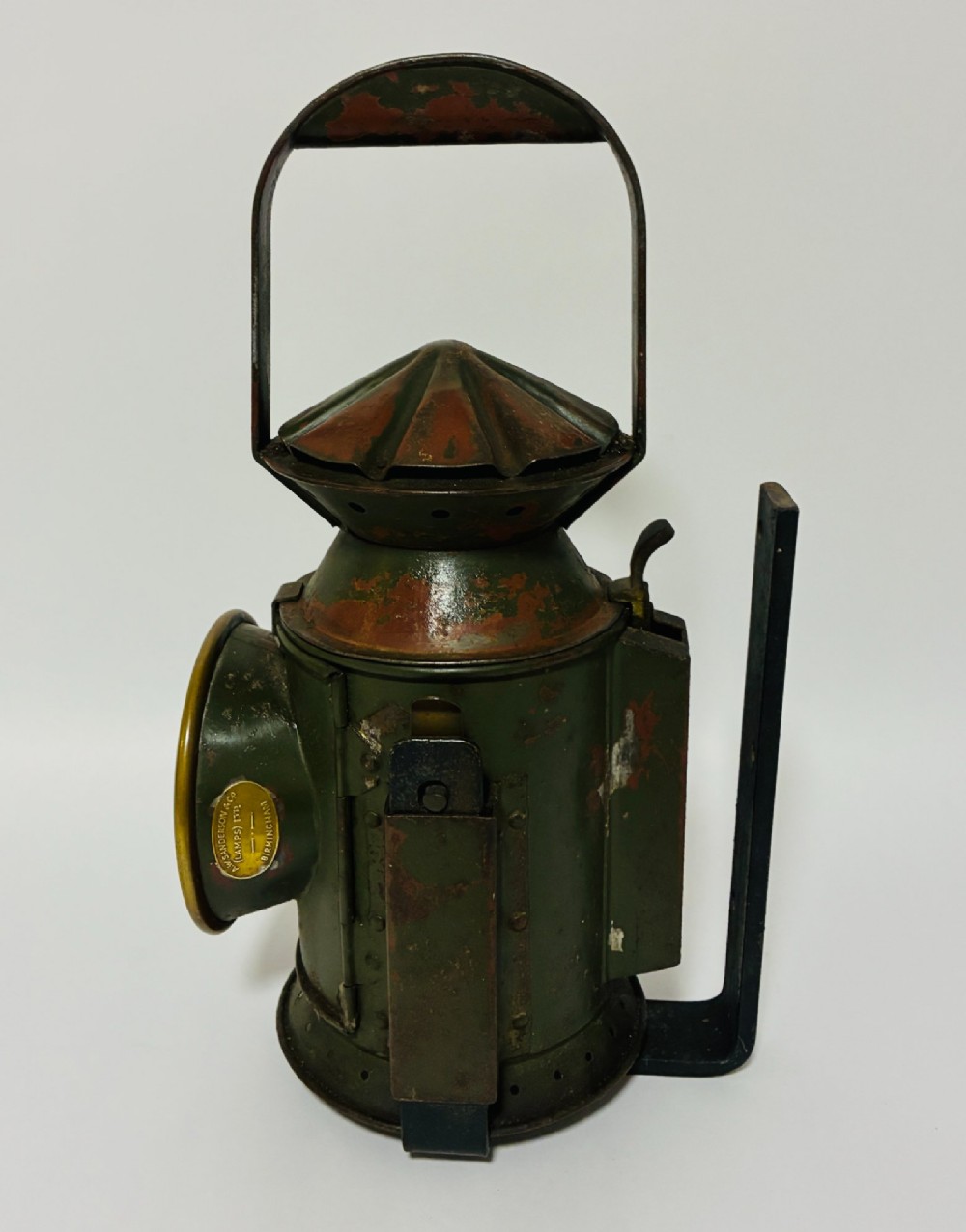 A vintage olive green painted metal railway signal lamp featuring a large round glass lens with a brass rim and a tall arched carrying handle. View IV