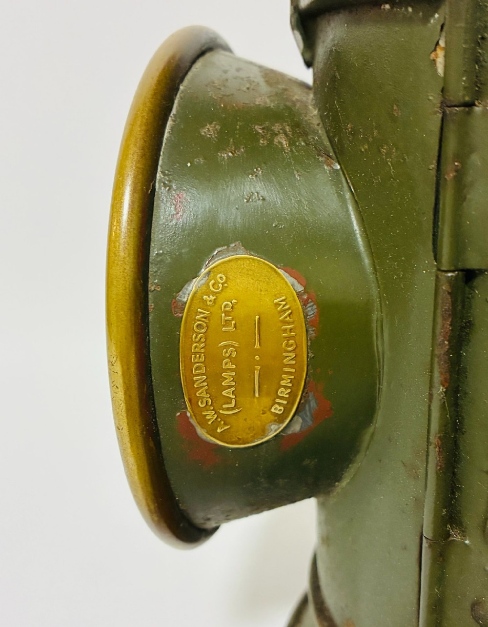 A vintage olive green painted metal railway signal lamp featuring a large round glass lens with a brass rim and a tall arched carrying handle. View V