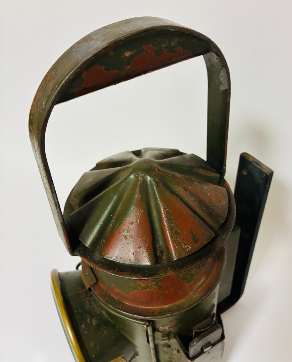 A vintage olive green painted metal railway signal lamp featuring a large round glass lens with a brass rim and a tall arched carrying handle. View VII