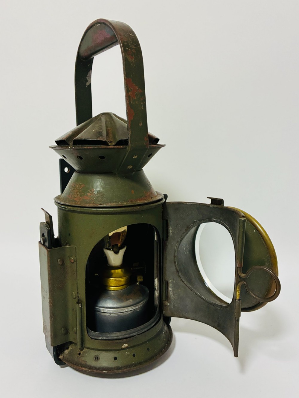 A vintage olive green painted metal railway signal lamp featuring a large round glass lens with a brass rim and a tall arched carrying handle. View VIII