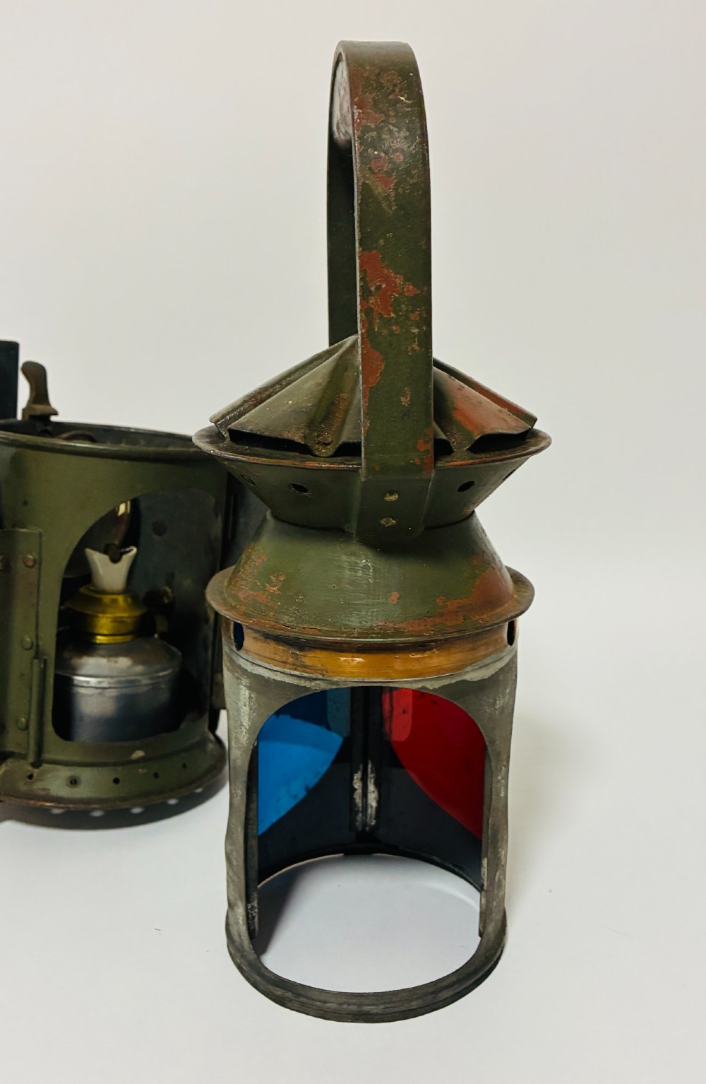 A vintage olive green painted metal railway signal lamp featuring a large round glass lens with a brass rim and a tall arched carrying handle. View XI