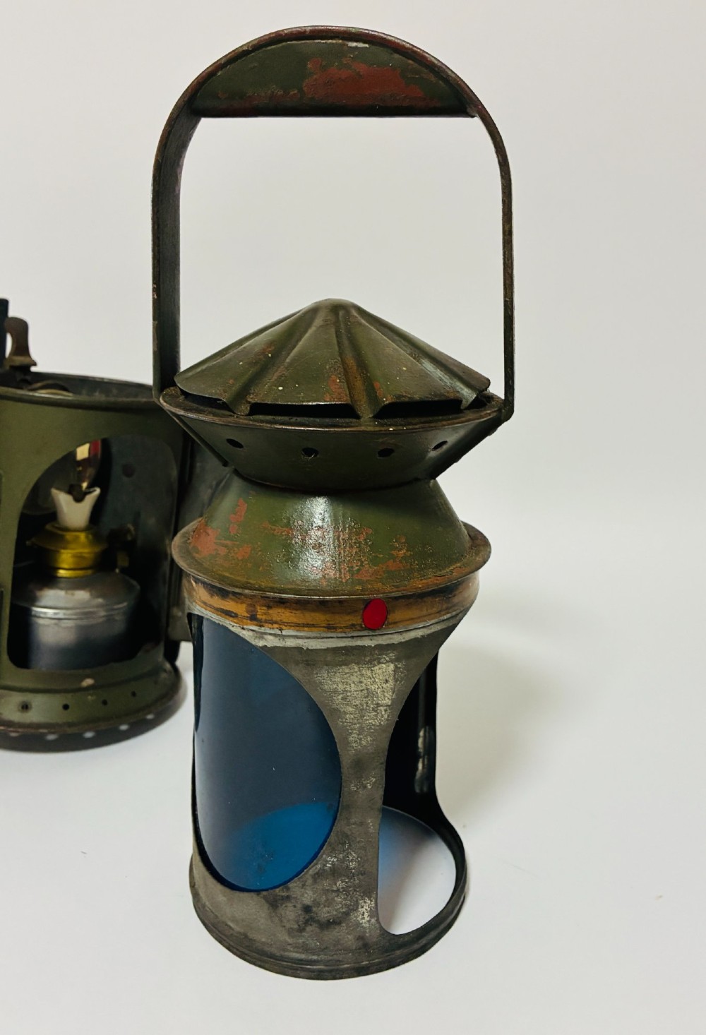 A vintage olive green painted metal railway signal lamp featuring a large round glass lens with a brass rim and a tall arched carrying handle. View XII