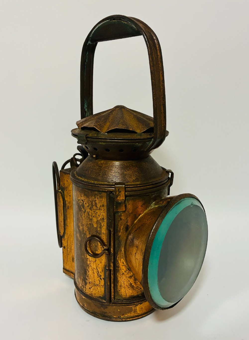 An antique metal railway signalling lamp with an arched top carrying handle, a conical vented cap, and a prominent circular glass lens.