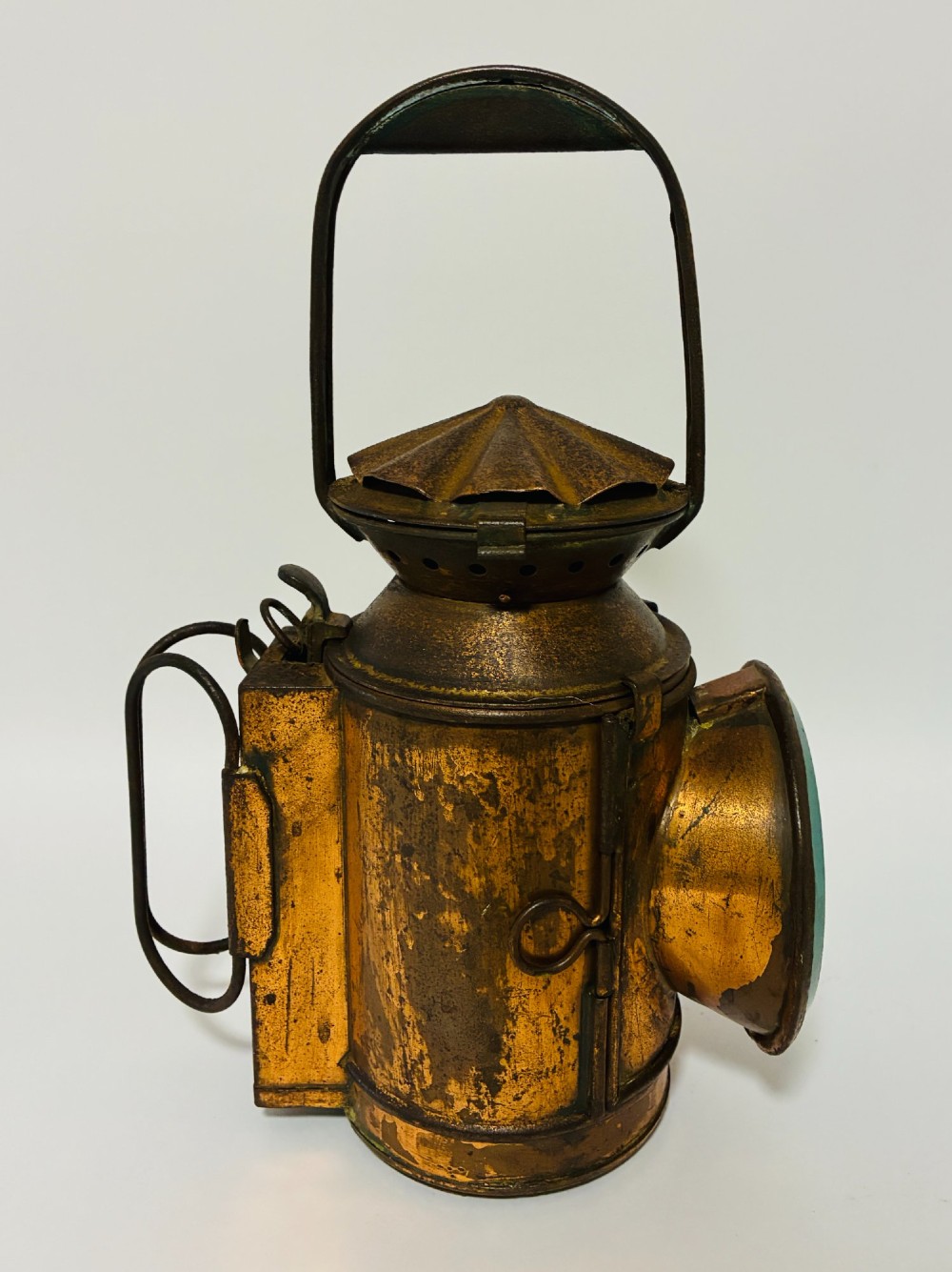An antique metal railway signalling lamp with an arched top carrying handle, a conical vented cap, and a prominent circular glass lens. View II