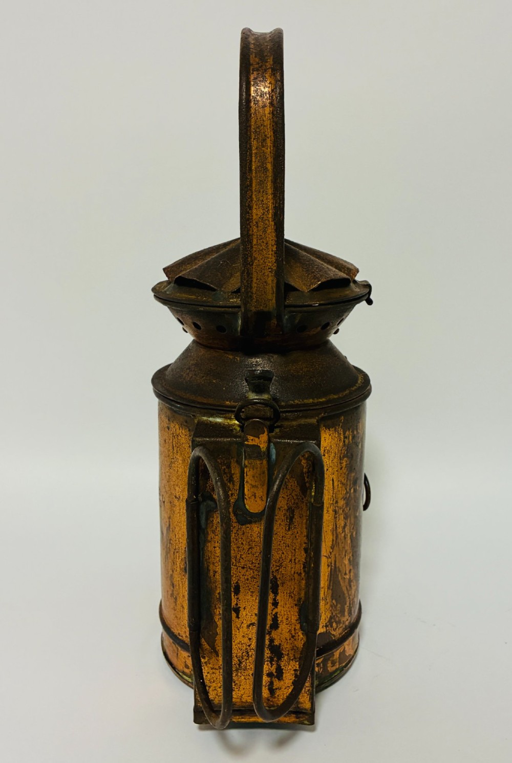 An antique metal railway signalling lamp with an arched top carrying handle, a conical vented cap, and a prominent circular glass lens. View III