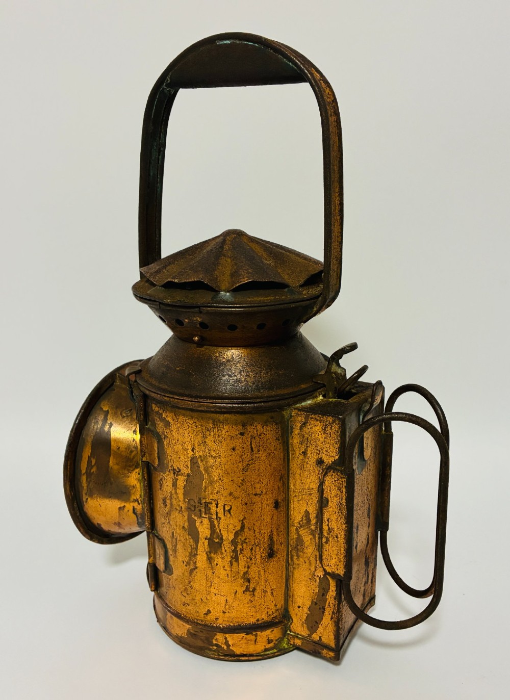 An antique metal railway signalling lamp with an arched top carrying handle, a conical vented cap, and a prominent circular glass lens. View IV