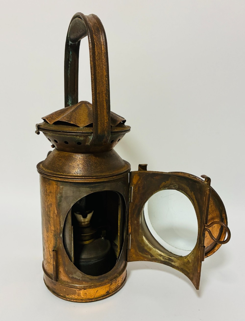 An antique metal railway signalling lamp with an arched top carrying handle, a conical vented cap, and a prominent circular glass lens. View IX