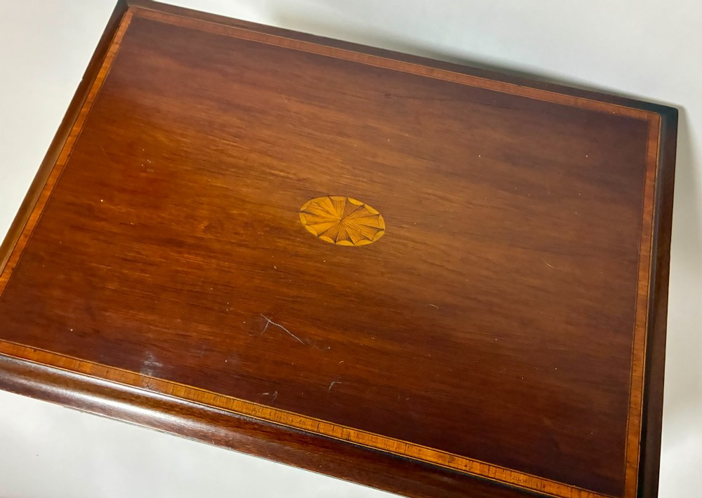 An Edwardian warm brown mahogany collectors box featuring wood inlay, brass drop handles, and a polished lid. View XV
