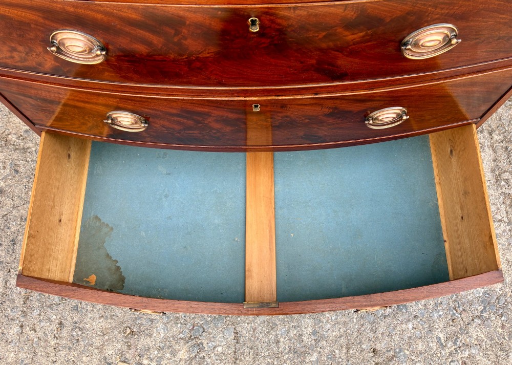 An antique Regency mahogany chest of drawers featuring a curved bowfront shape, three drawers with oval brass handles, and splayed bracket feet. View VIII