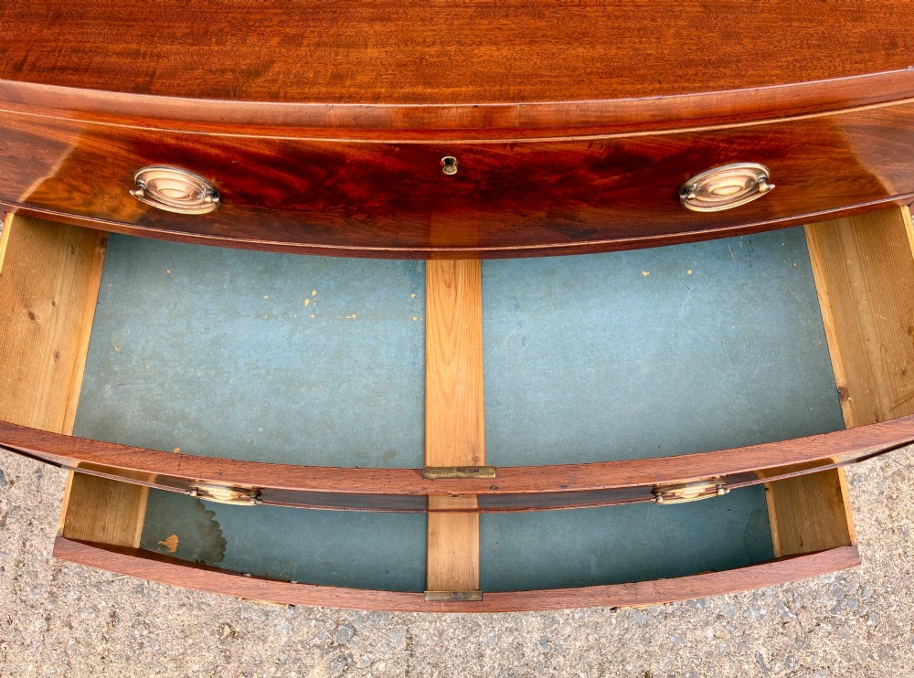 An antique Regency mahogany chest of drawers featuring a curved bowfront shape, three drawers with oval brass handles, and splayed bracket feet. View IX