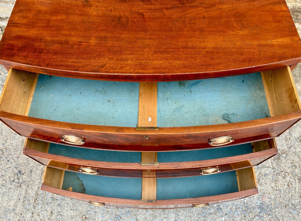 An antique Regency mahogany chest of drawers featuring a curved bowfront shape, three drawers with oval brass handles, and splayed bracket feet. View X