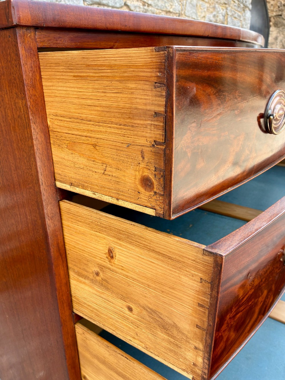 An antique Regency mahogany chest of drawers featuring a curved bowfront shape, three drawers with oval brass handles, and splayed bracket feet. View XI