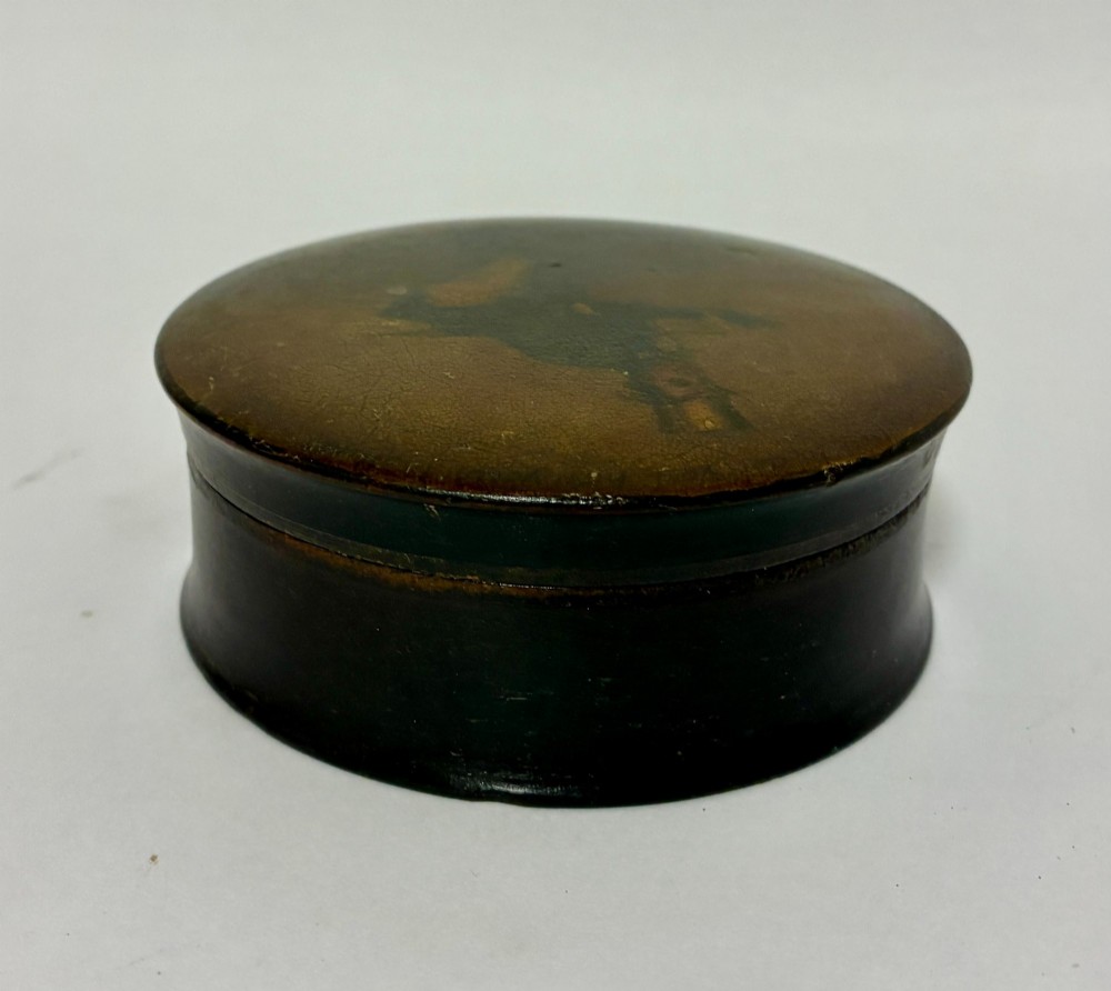 A circular Georgian papier-mache table snuff box featuring a hand-painted depiction of a gentleman in a top hat and tailcoat against a dark lacquered background. View V