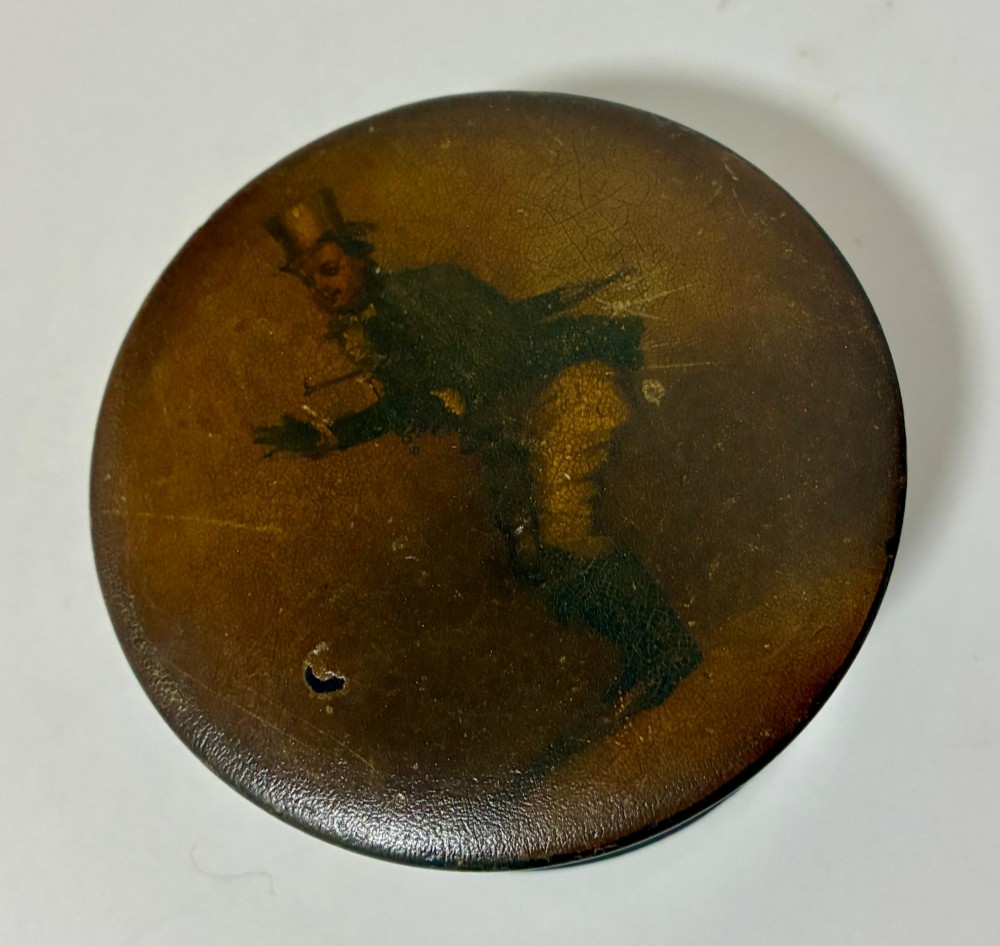 A circular Georgian papier-mache table snuff box featuring a hand-painted depiction of a gentleman in a top hat and tailcoat against a dark lacquered background. View VIII