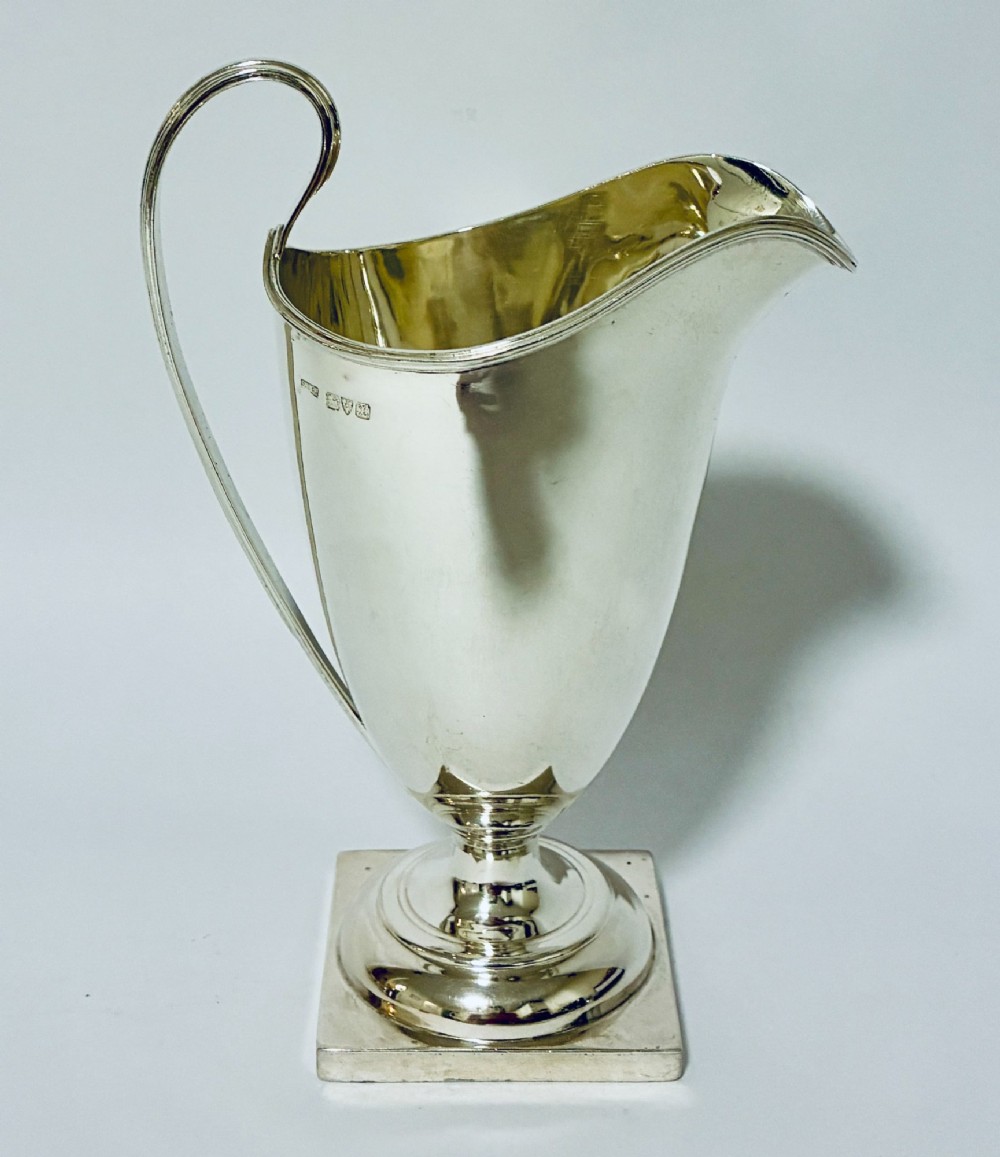 A sterling silver helmet-shaped cream jug featuring a high loop handle, side hallmarks, and a square plinth base.