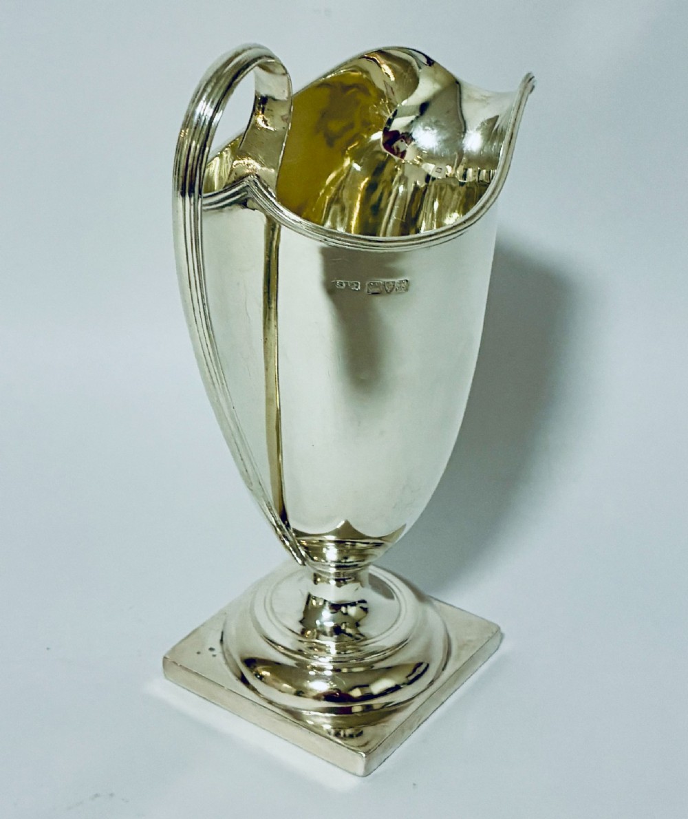A sterling silver helmet-shaped cream jug featuring a high loop handle, side hallmarks, and a square plinth base. View II