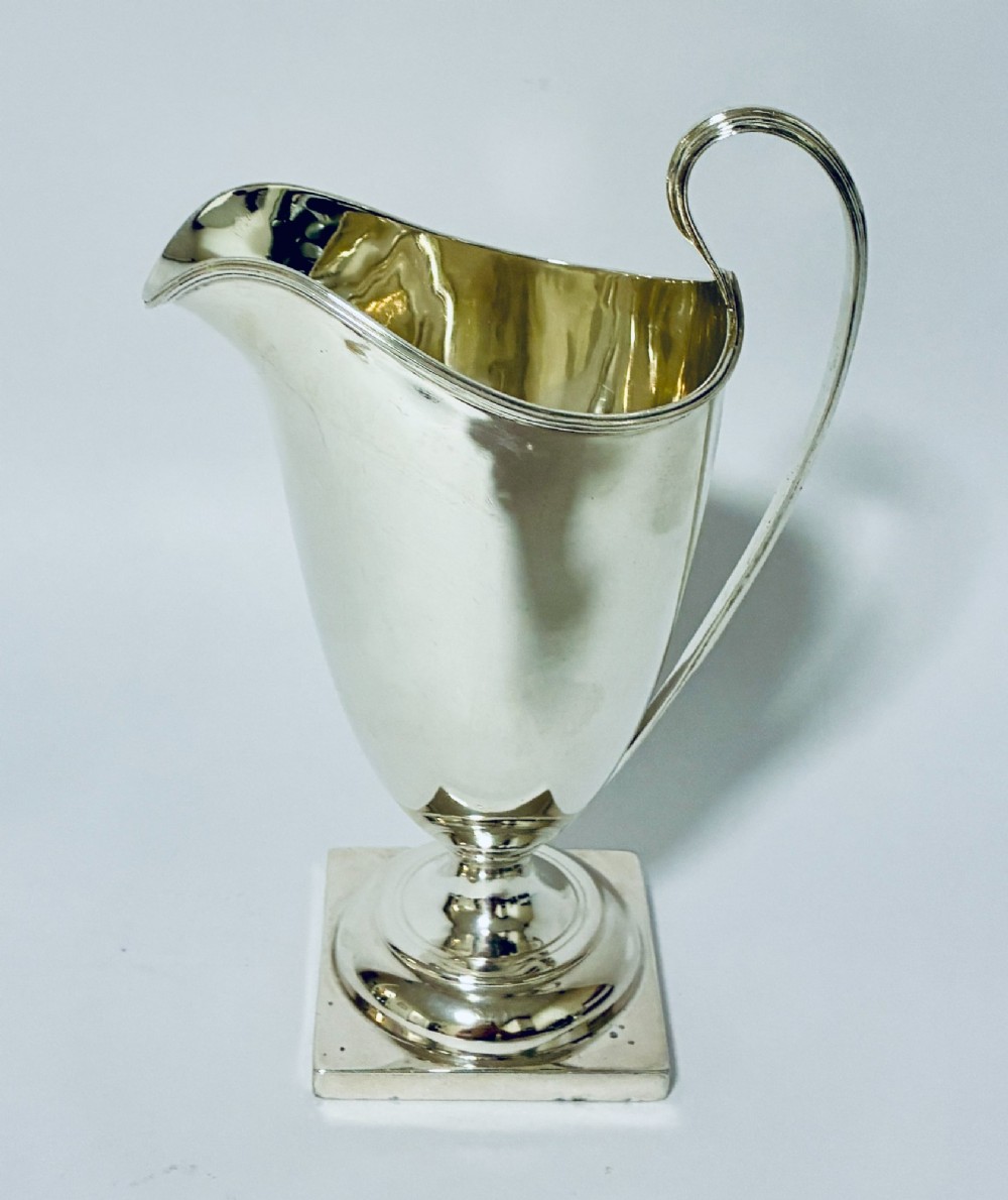 A sterling silver helmet-shaped cream jug featuring a high loop handle, side hallmarks, and a square plinth base. View IV