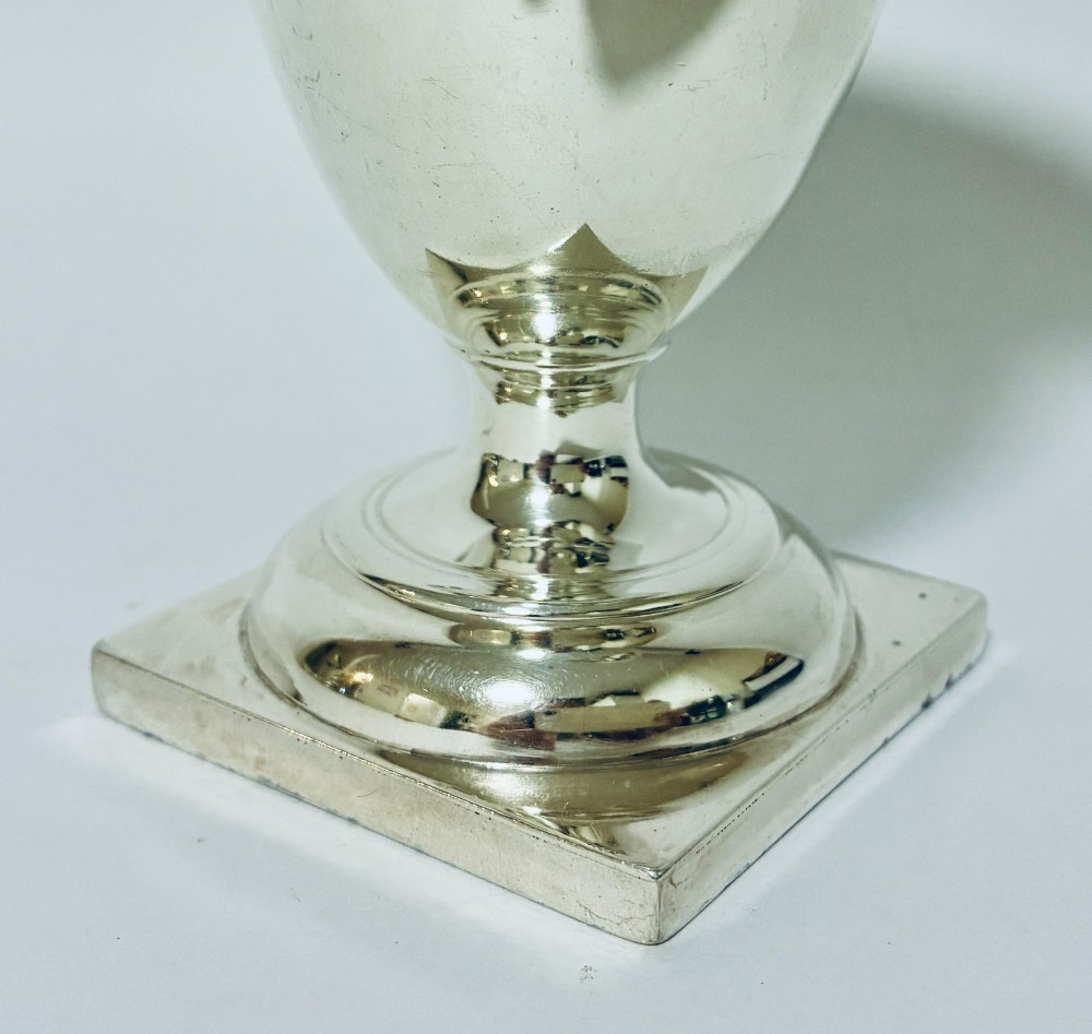 A sterling silver helmet-shaped cream jug featuring a high loop handle, side hallmarks, and a square plinth base. View VII