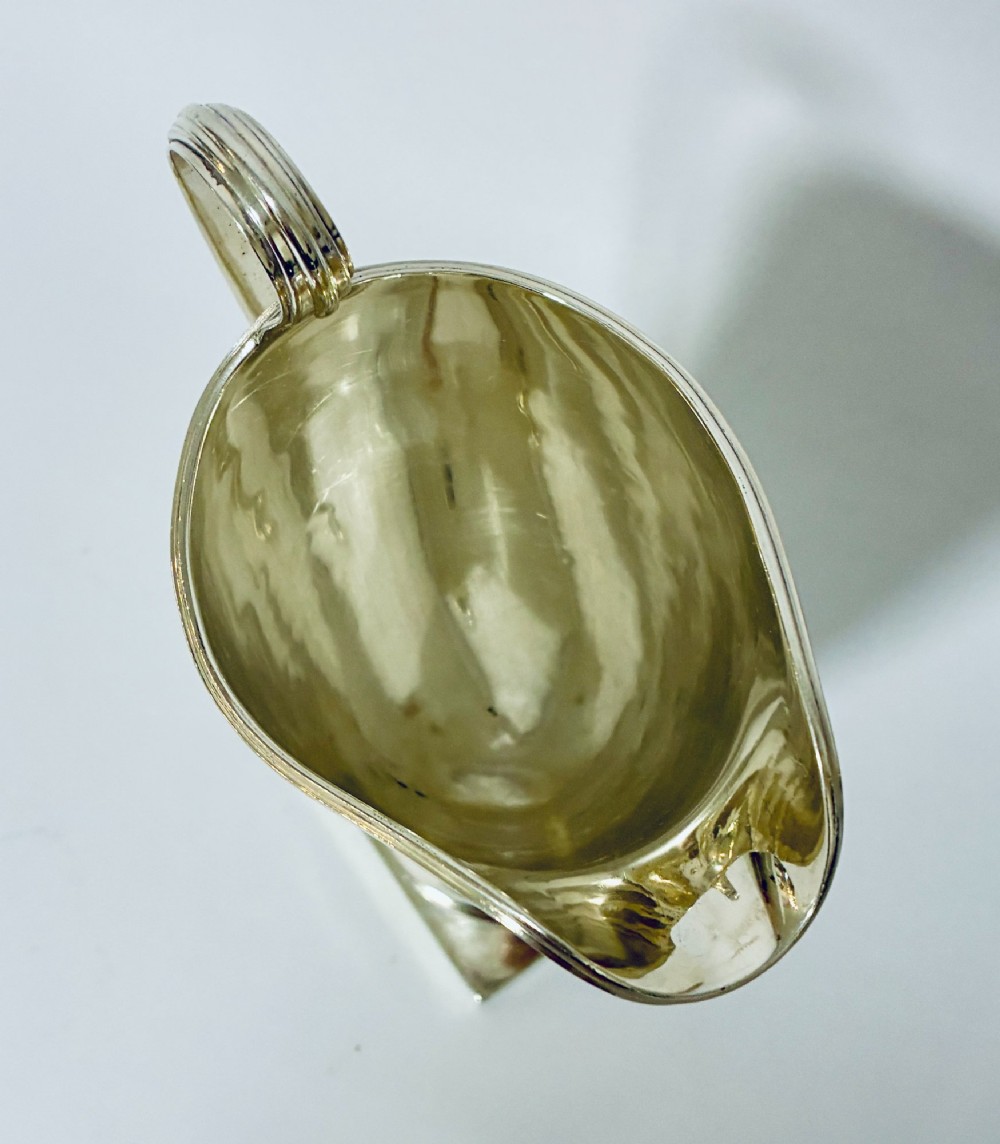 A sterling silver helmet-shaped cream jug featuring a high loop handle, side hallmarks, and a square plinth base. View VIII
