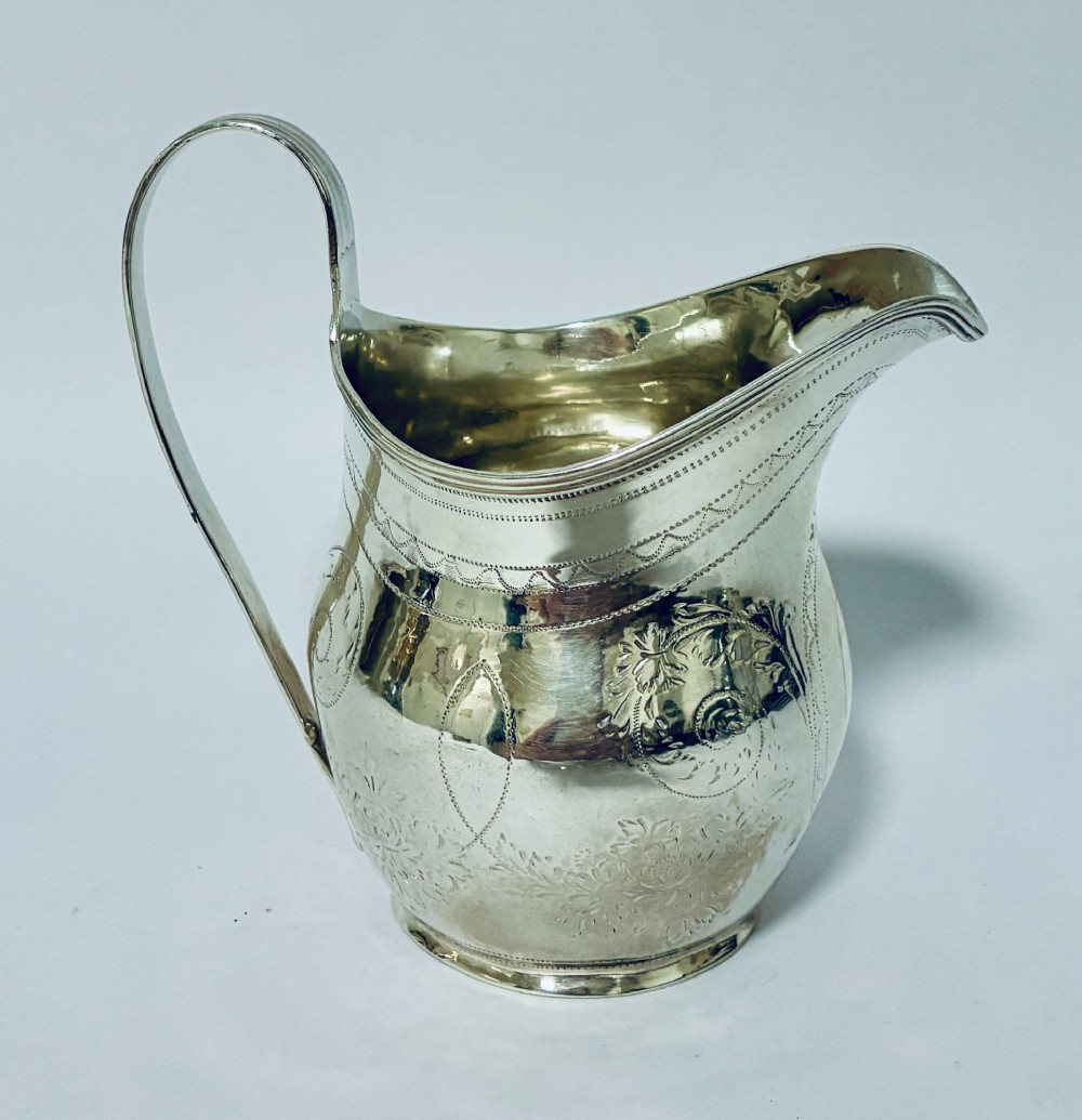 A Georgian sterling silver cream jug featuring a high loop handle, a shaped spout, and fine floral engraving across the body.
