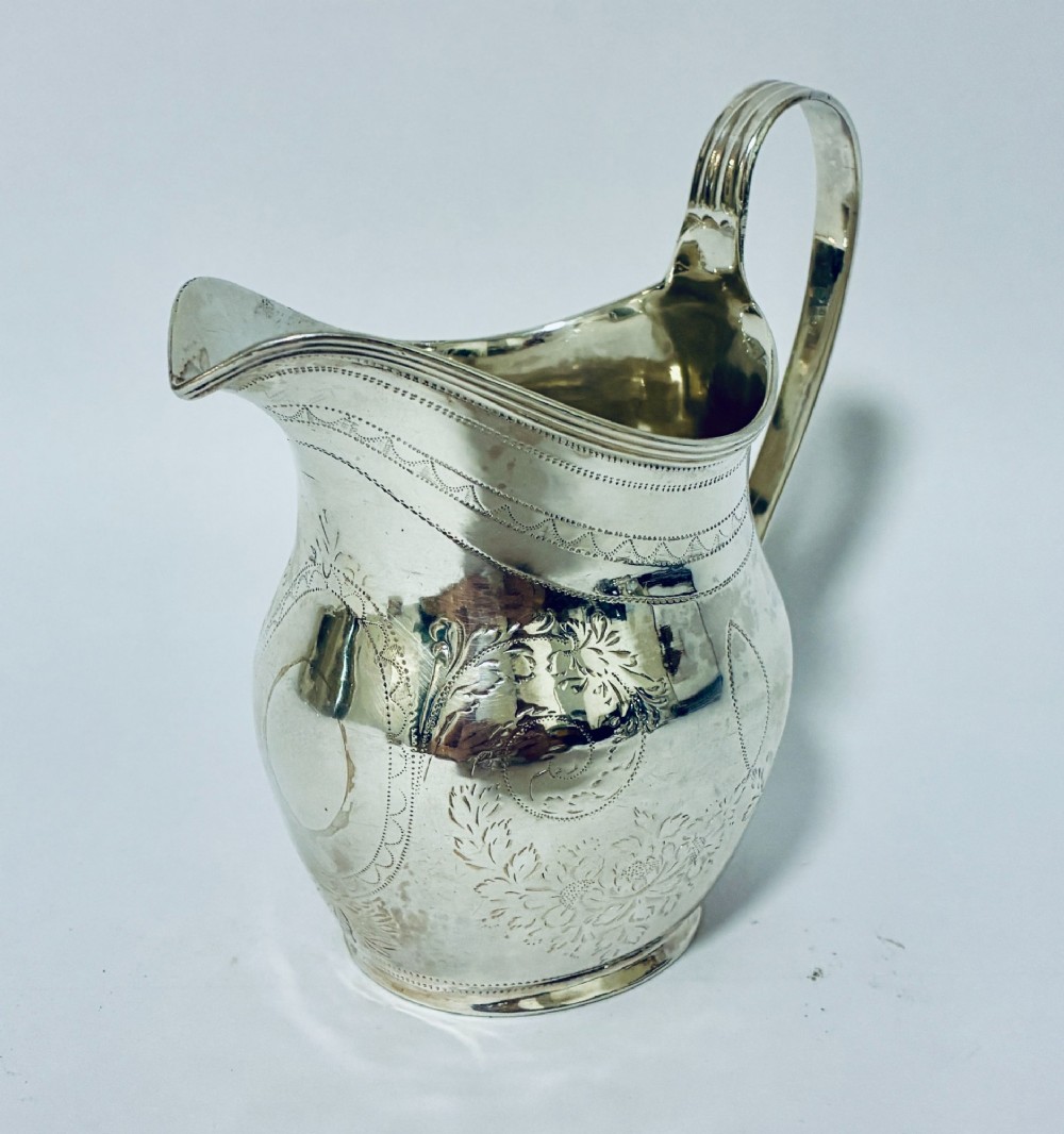 A Georgian sterling silver cream jug featuring a high loop handle, a shaped spout, and fine floral engraving across the body. View III