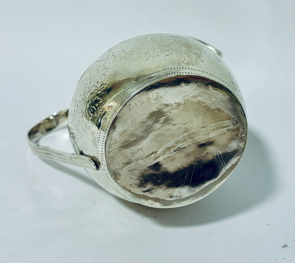 A Georgian sterling silver cream jug featuring a high loop handle, a shaped spout, and fine floral engraving across the body. View VII