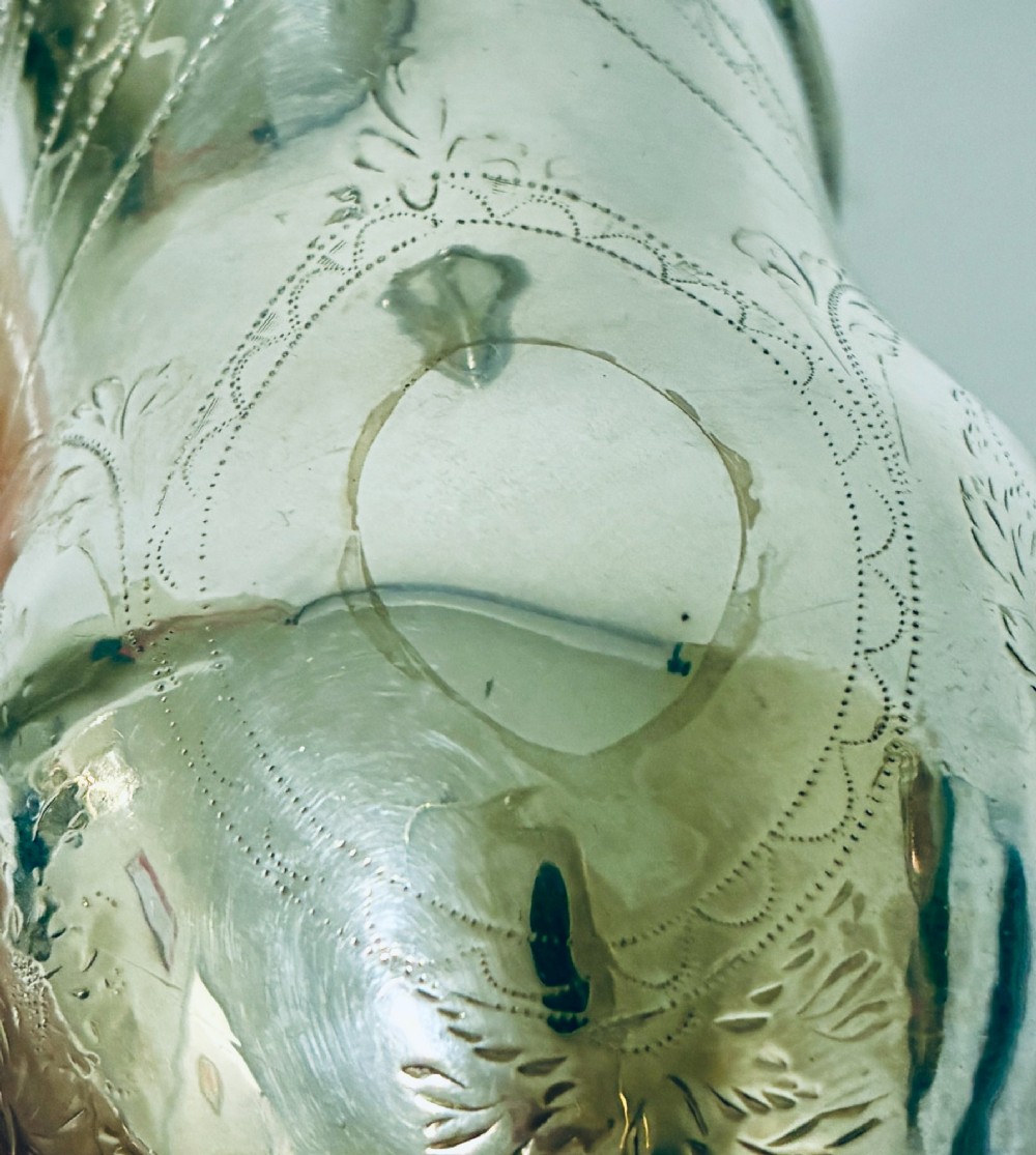 A Georgian sterling silver cream jug featuring a high loop handle, a shaped spout, and fine floral engraving across the body. View VIII