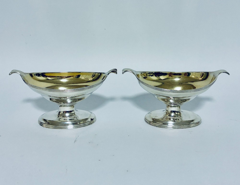 A pair of Georgian sterling silver boat-shaped salt cellars with pedestal bases and gilded interiors.