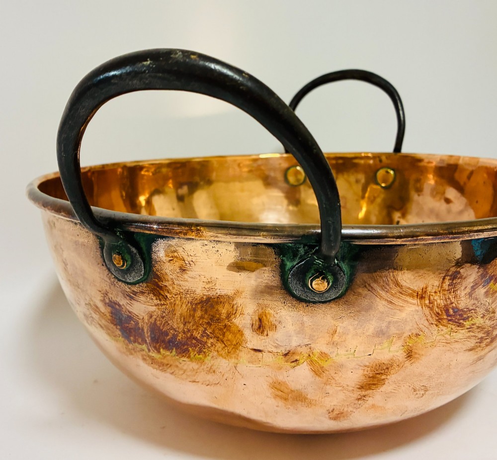 A round antique copper bowl with a wide rim and two black wrought iron handles attached with copper rivets. View VI