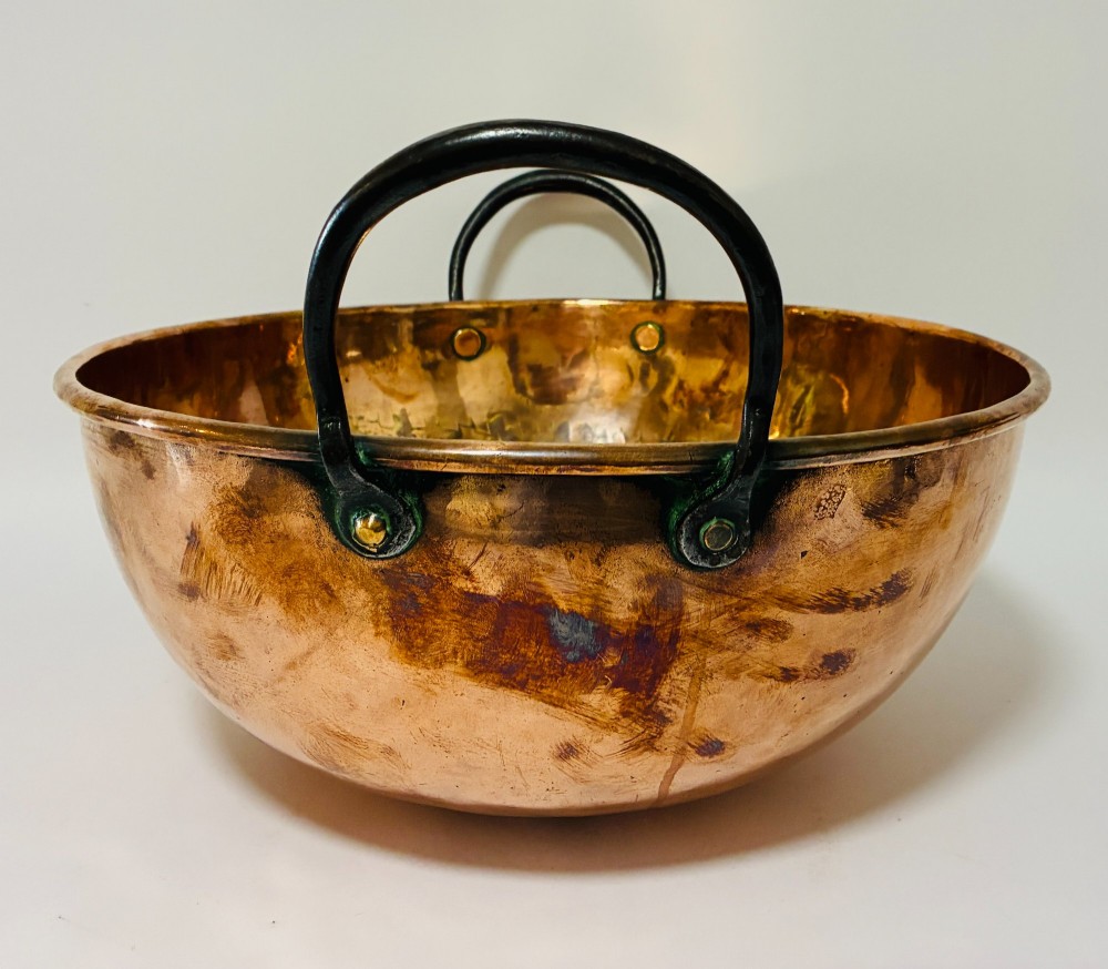 A round antique copper bowl with a wide rim and two black wrought iron handles attached with copper rivets. View VII