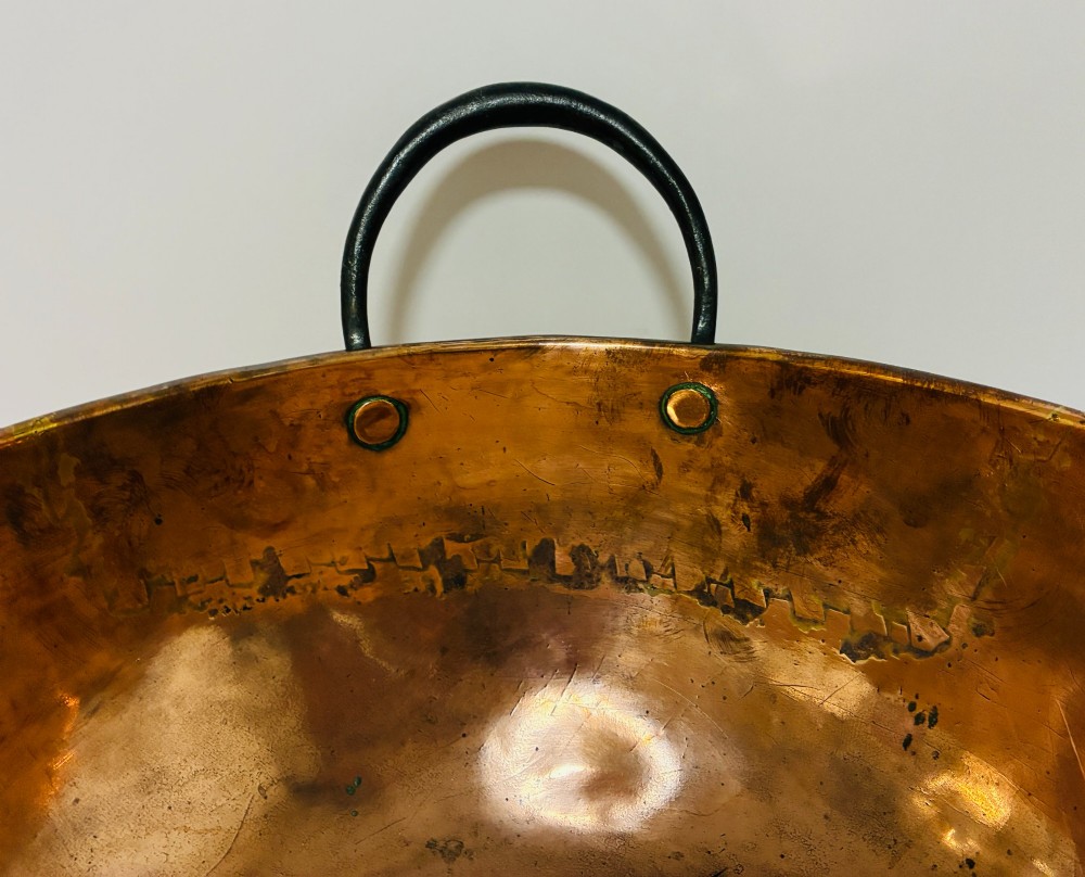 A round antique copper bowl with a wide rim and two black wrought iron handles attached with copper rivets. View VIII