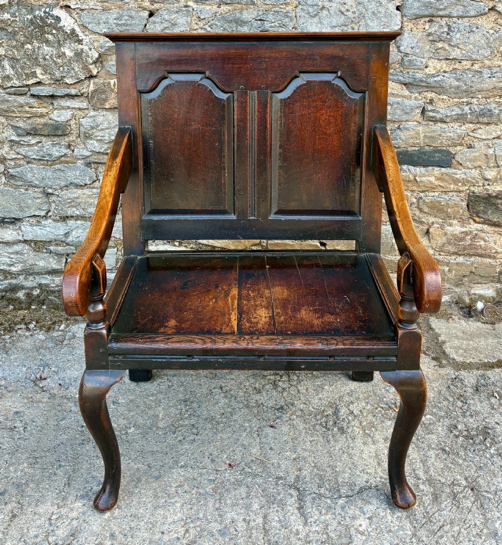 An 18th-century Georgian dark oak settle featuring a twin arched-panel back, contoured armrests, and cabriole front legs.