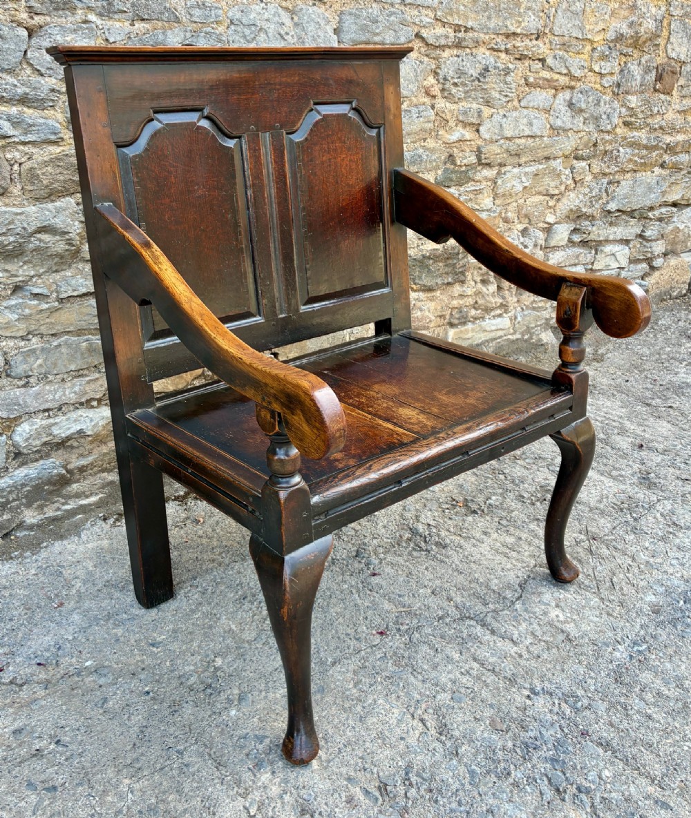 An 18th-century Georgian dark oak settle featuring a twin arched-panel back, contoured armrests, and cabriole front legs. View IV