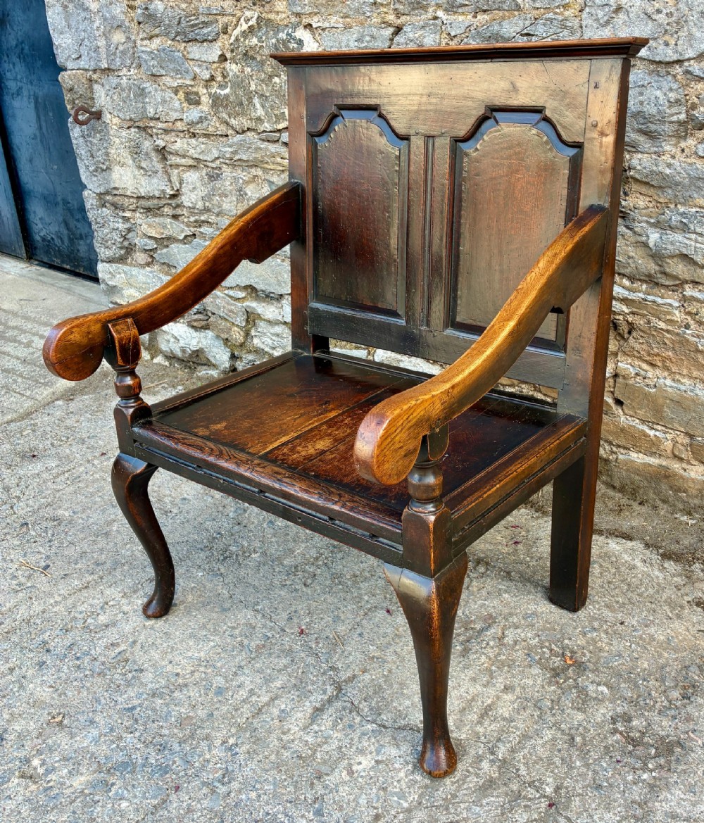 An 18th-century Georgian dark oak settle featuring a twin arched-panel back, contoured armrests, and cabriole front legs. View V