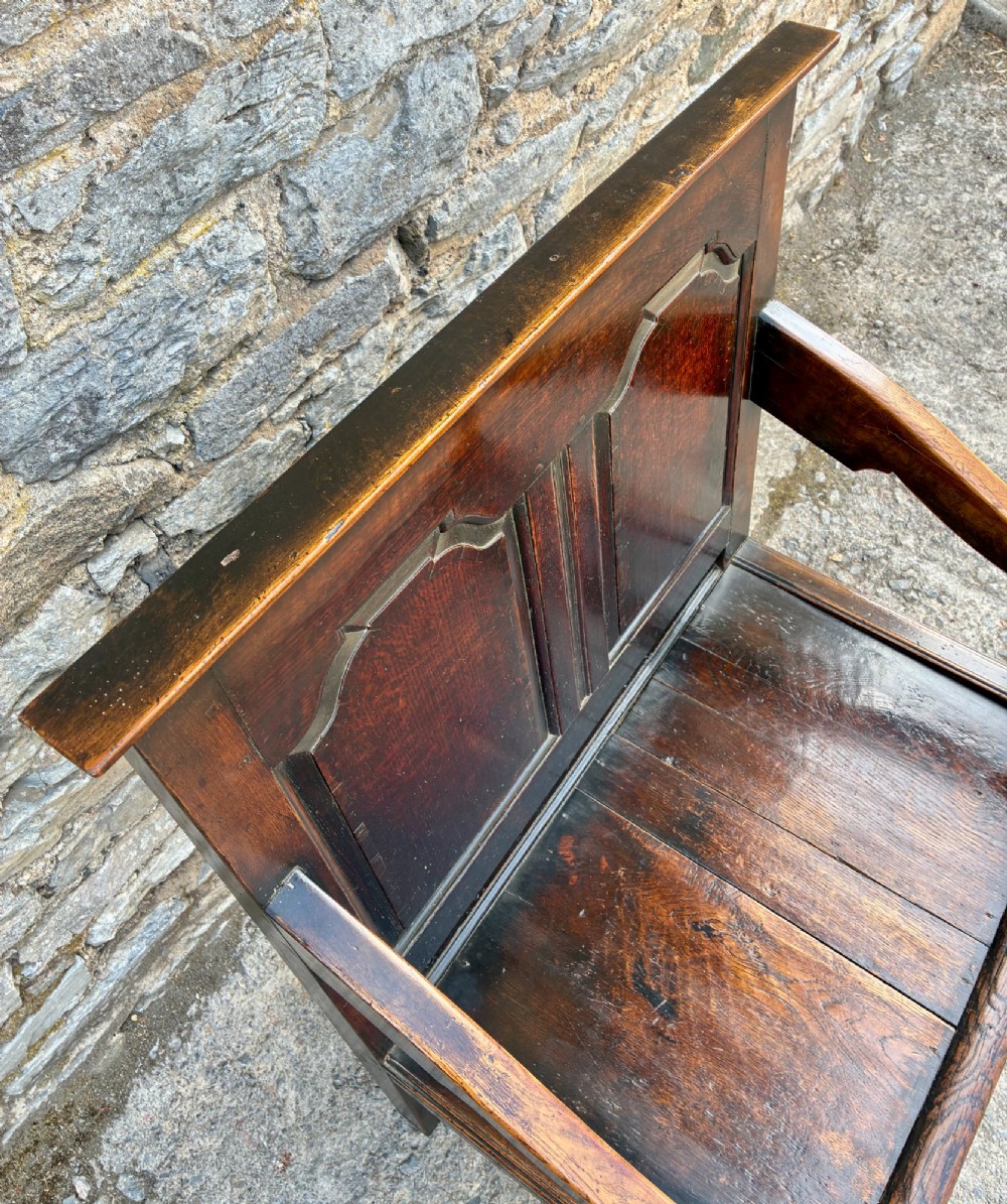 An 18th-century Georgian dark oak settle featuring a twin arched-panel back, contoured armrests, and cabriole front legs. View X