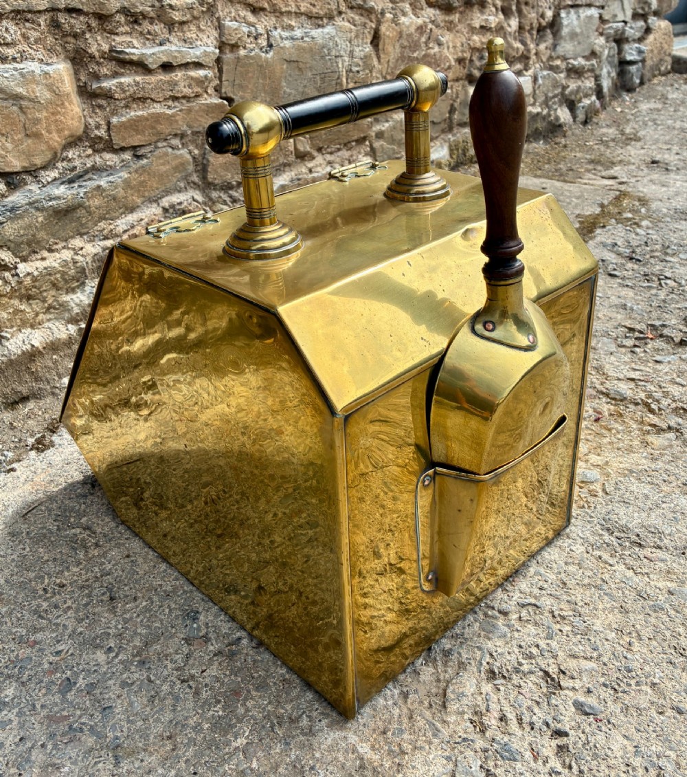 An antique brass sloped coal scuttle featuring a turned wooden carrying handle, a hinged lid, and an attached brass shovel at the rear. View VII