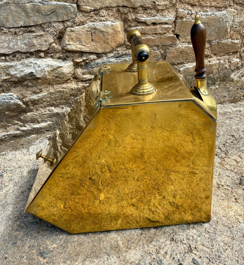 An antique brass sloped coal scuttle featuring a turned wooden carrying handle, a hinged lid, and an attached brass shovel at the rear. View VIII