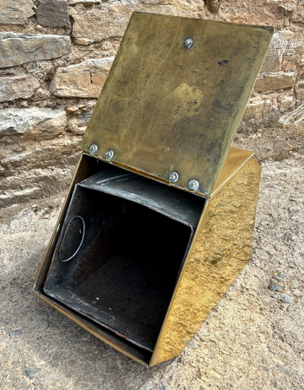 An antique brass sloped coal scuttle featuring a turned wooden carrying handle, a hinged lid, and an attached brass shovel at the rear. View X